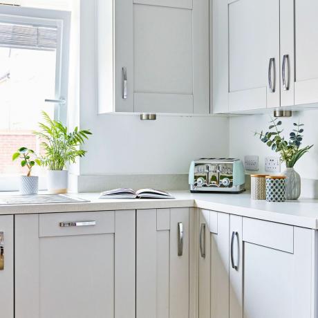 Beyaz boyalı mutfak ve mavi ekmek kızartma makinesi ve beyaz tezgah üzerinde sergilenen vazolar ile beyaz dolaplar