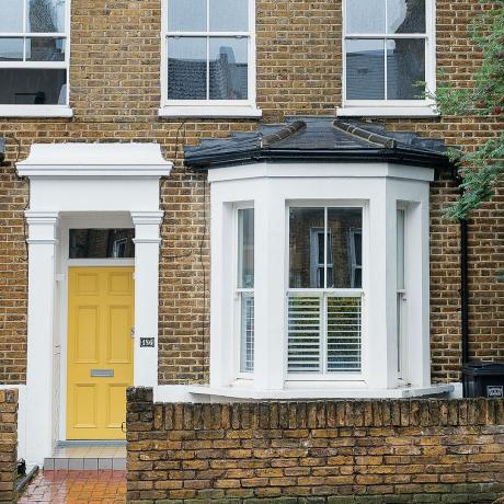 ภายนอกบ้านที่มีประตูหน้าบ้านสีเหลืองและหน้าต่างที่ยื่นจากผนัง