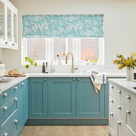 Valkoinen keittiö, jossa siniset kaapistot ja kukkaverhot