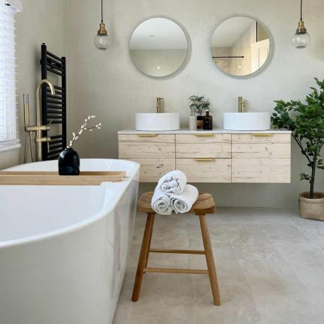 neutralt badeværelse med fritstående badekar, trævask med dobbelt håndvask og spejle og guldhaner