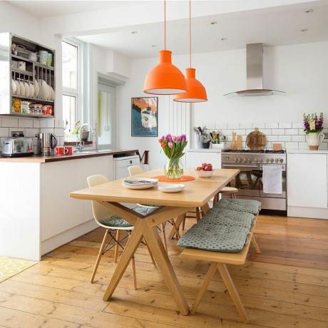 Fehér konyha fa padlóval, narancssárga függőlámpákkal, asztallal és székekkel