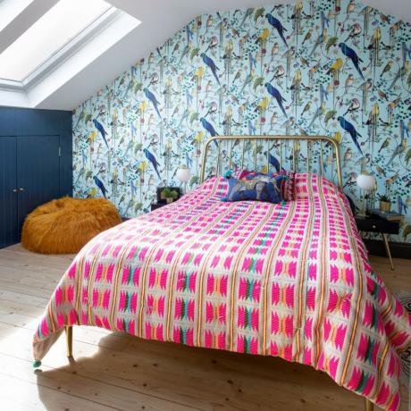 Bēniņu guļamistaba ar putnu apdrukas tapetēm aiz gultas