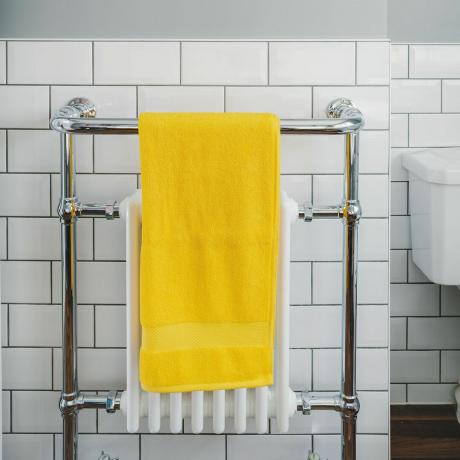 vonios kambarys su geltonu rankšluosčiu, pakabintu ant rankšluosčių radiatoriaus