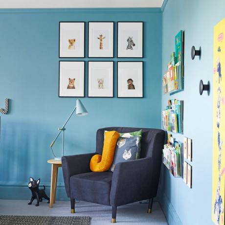 dětský pokoj s tmavě modrým křeslem a modrými stěnami s zarámovaným nástěnným uměním