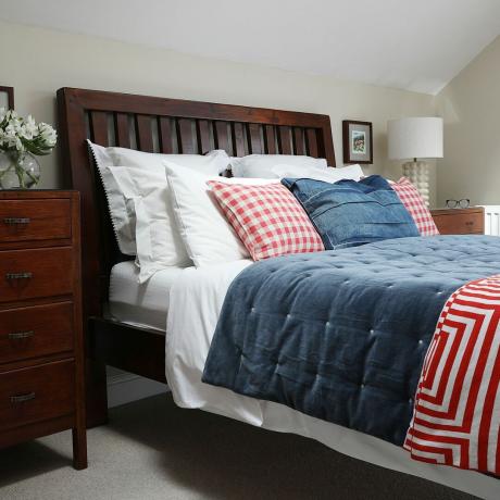 Sovrum med sovrumsmöbler i trä och röda, vita och blå kuddar och överkast