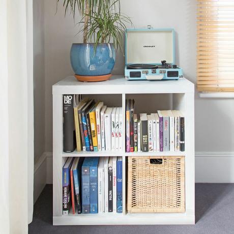 unidade de armazenamento branca com livros e uma cesta e planta e toca-discos em cima