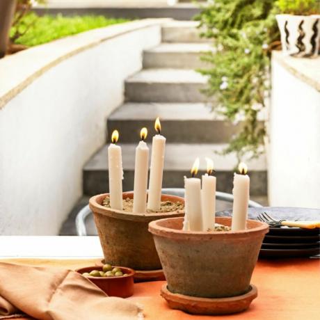 테라코타 화분을 사용하여 간단한 파티오 디스플레이, 그릇과 칼붙이가 있는 야외 테이블, 오래된 테라코타 화분에 불이 켜진 양초를 만드는 양초 재배자.