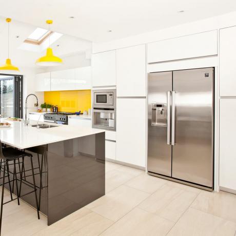 Hvitt kjøkken med dobbel sølv amerikansk kjøleskap med fryser, øy og gule pendellamper