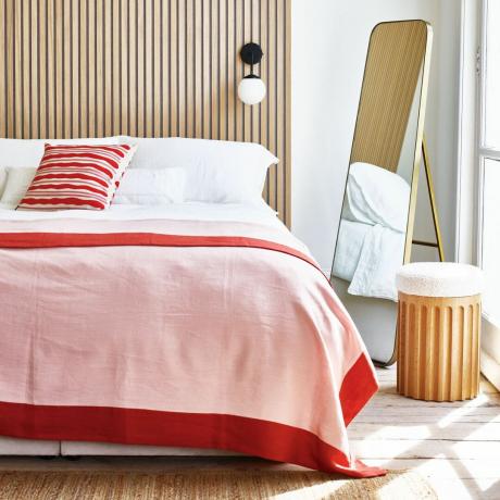 غرفة نوم مع لوح أمامي مكسو بألواح خشبية ومفرش سرير باللونين الأحمر والوردي