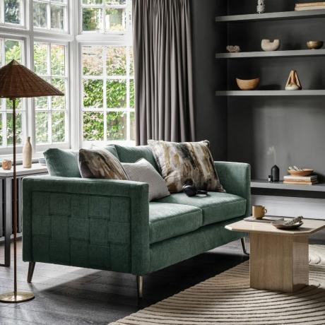 Зеленый рельефный диван в темной гостиной с подушками, журнальным столиком, лампой, стеллажом