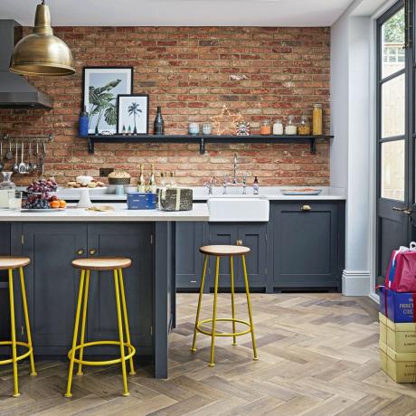 Cocina con gabinetes de color gris oscuro, pisos de madera de parquet, taburetes de bar y paredes de ladrillo a la vista