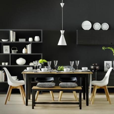 Salle à manger entièrement noire avec table peinte en noir, chaises et accessoires blancs