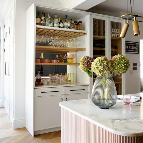 armário de bebidas branco com bancada em ilha de cozinha oposta com vaso de flores
