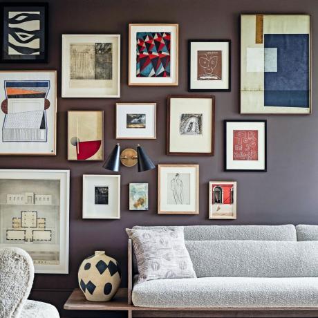 Sala de estar com sofá e cadeira, carpete no piso de madeira e parede de galeria repleta de obras de arte