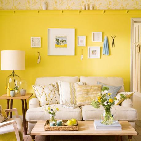 غرفة معيشة صفراء مع أريكة كريمية وجدار معرض