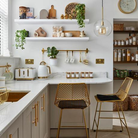 Кухня со светлой мебелью, белой рабочей поверхностью и золотыми металлическими аксессуарами.