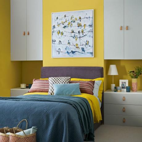Dormitorio de color amarillo brillante con unidades de almacenamiento de IKEA en los nichos a cada lado de una cama doble