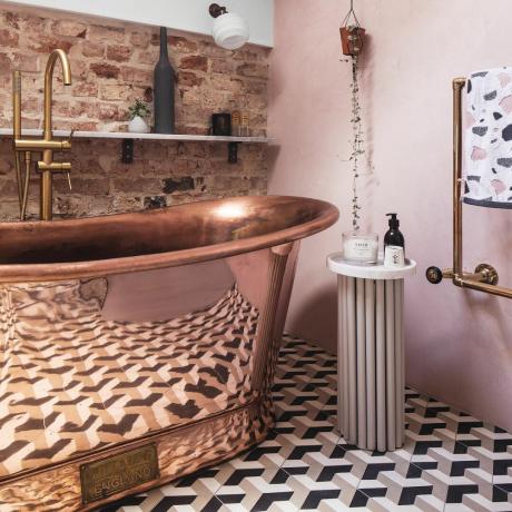bagno rosa con vasca in rame e muro di mattoni