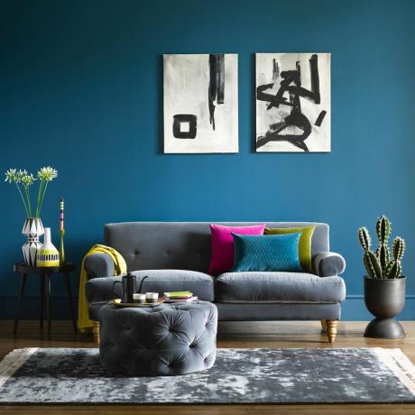 Синьо боядисана стена за всекидневна с елегантен сив диван и абстрактни произведения на изкуството