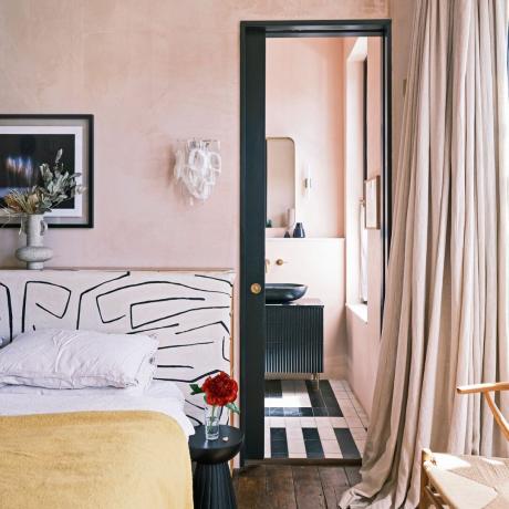 vaaleanpunainen makuuhuone, jossa on oma kylpyhuone, kuviollinen sängynpääty ja pitkät verhot