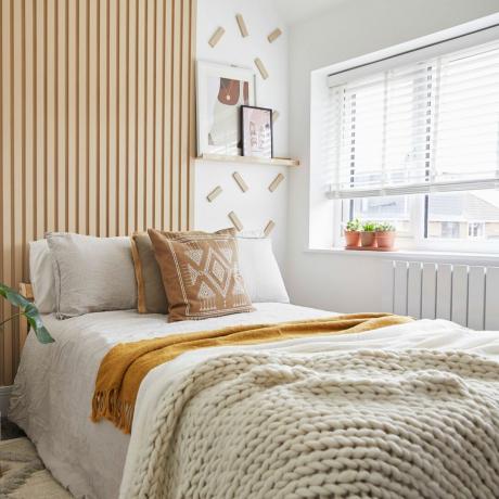 kamar tidur netral dengan panel kayu linier di dinding putih dan rak pajangan tipis di sampingnya