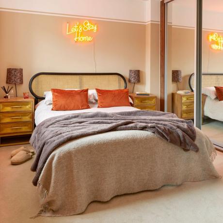 Soveværelse med sengegavl i rattan, neutralt farvede plader og neonskilt over sengen
