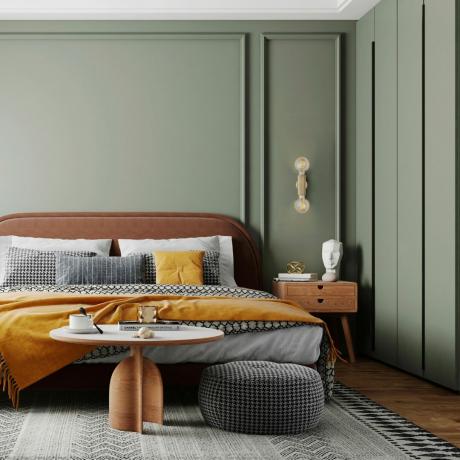 작은 침실 색상 아이디어, 녹색 패널 벽이 있는 녹색 침실, 단색 침구가 있는 가죽 침대, 푸프 및 러그. 나무 사이드 테이블과 커피 테이블, 사프란 던지기와 쿠션, 나무 바닥
