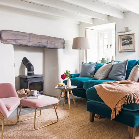 Una sala de estar de cabaña de techo bajo con sofá de terciopelo azul y estufa de leña - Colin Poole