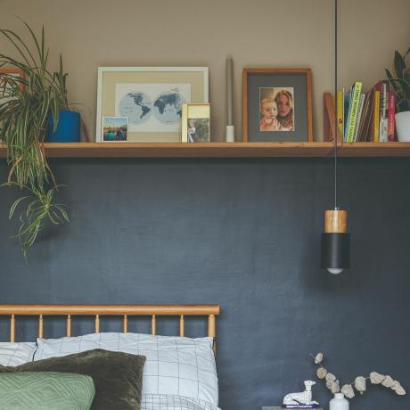 ベッドの後ろのグレーとネイビーブルーの壁は、額縁、本、植物のある棚で区切られています