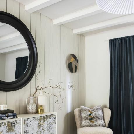 Specchio rotondo con cornice nera su parete rivestita di pannelli bianchi