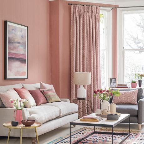 Dzīvojamās istabas aizkars ar persiku sienām, krēmkrāsas dīvāns un rozā aizkari