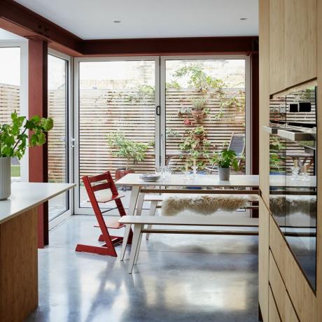 ruang makan dapur terbuka dengan pintu bifold dan meja makan dengan kursi tinggi Tripp Trapp merah