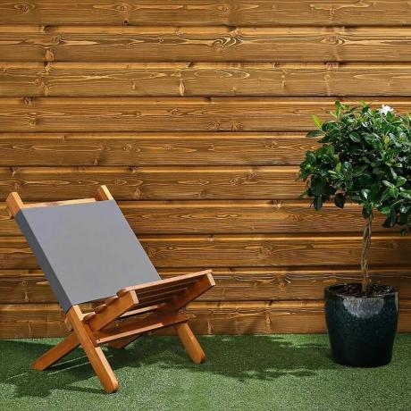 Sötét fa kültéri burkolat a falon kerti székkel és fűvel.