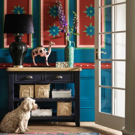 idéias de decoração de parede de corredor, corredor azul com painéis impressos à mão, console pintado de azul marinho com luminária, vaso, enfeites, piso de madeira, tapete, porta aberta