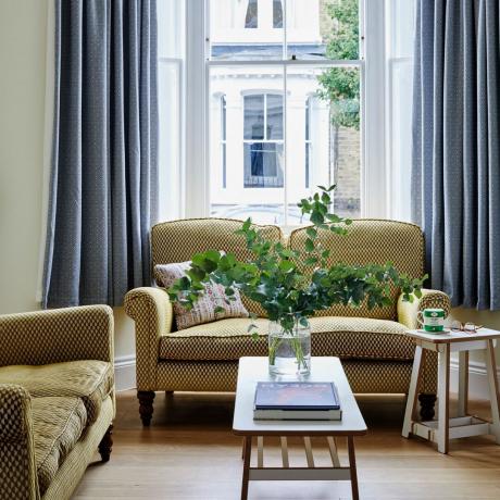 ruang tamu tradisional yang cerdas dengan sofa bermotif mustard, meja kopi Ercol, dan tirai biru