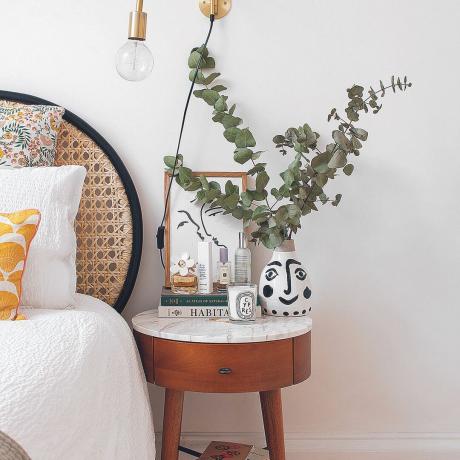 Camera da letto di Kate Spires con testiera in rattan e comodino della metà del secolo con eucalipto in cima.