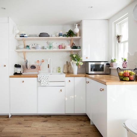bílá kuchyně s dřevěnými pracovními deskami a měděnými úchyty
