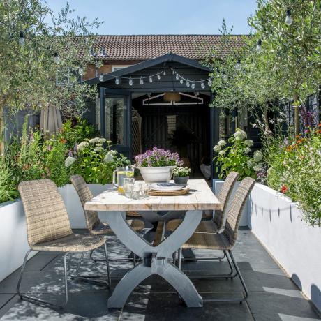 wąski ogród z jadalnią przed malowaną szopą altanką