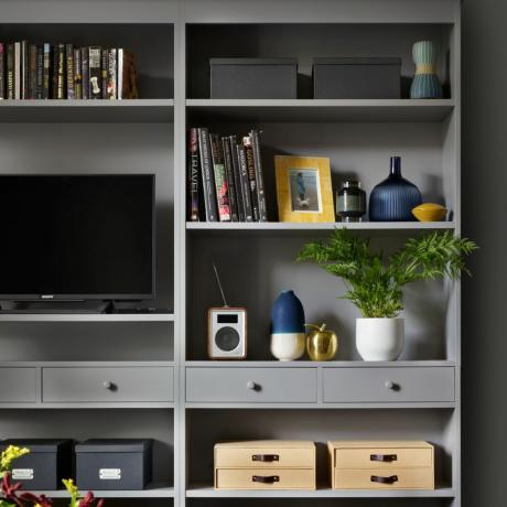 Tamsiai pilka lentyna su televizoriumi ir daiktadėžėmis svetainėje