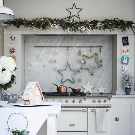 Wit ovenfornuis in de schoorsteenhaard versierd met verlichting, stervormen en bladeren, witte tafel met peperkoekhuisje op de tafel op de voorgrond