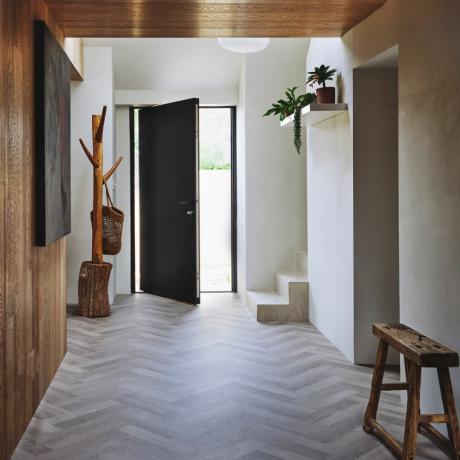 prieškambario sienų dekoro idėjos, platus šiuolaikiškas prieškambaris su lentyna su augalais, pilkos silkės grindys, viena medinė siena, viena balta, medinė kabykla, taburetė
