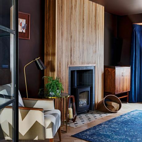 Уютно с черни рамкирани врати в стил Crittall, набраздени дървени детайли около печката на дърва, син килим, дървени шкафове и синя кадифена завеса декорация на прозорци
