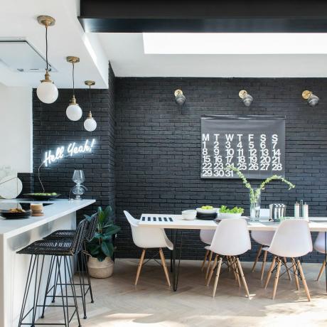 Melni krāsota ķieģeļu siena virtuves piebūves ēdamistabas zonā ar baltu pusdienu galdu un krēsliem
