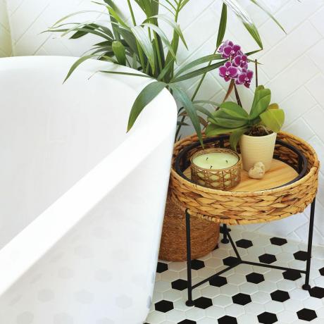 Hvidt fritstående badekar med vævet sidebord og sort/hvid klinkegulv