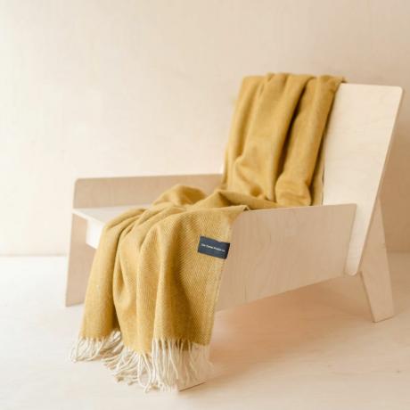 بطانية صغيرة من الصوف المعاد تدويره من الخردل متعرجة ملفوفة على كرسي خشبي