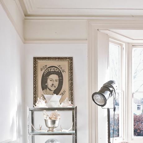 Baltie dzīvojamās istabas griesti ar karnīzi un karalienes mākslas darbi, kas karājas zemāk