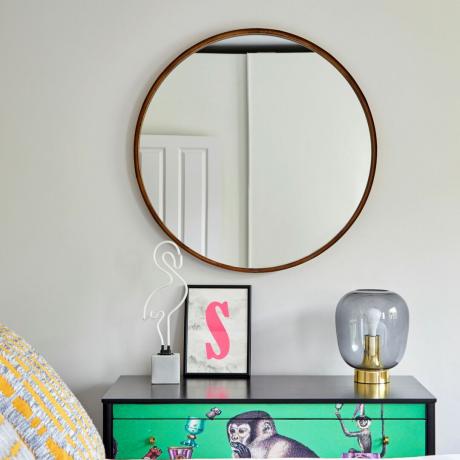 Ringikujuline rippuv peegel magamistoas kaunistatud musta kummuti kohal