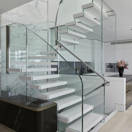 Bisca atvērtas kāpnes baltā, modernā mājā ar baltu virtuvi aiz tās