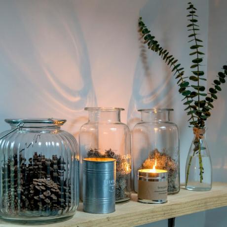 Деревянная полка со свечами и стеклянными вазами со мхом, сосновыми шишками и эвкалиптом.