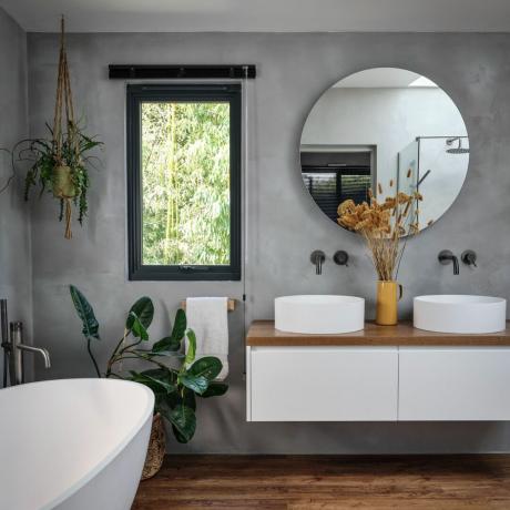 Badkamer met grijze muur, ligbad, twee wastafels en versierd met planten